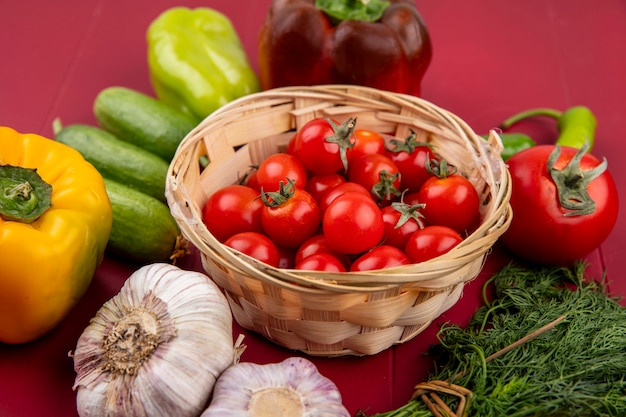 Вид сбоку на овощи как помидоры в корзине с перцем, чесноком и укропом на красном
