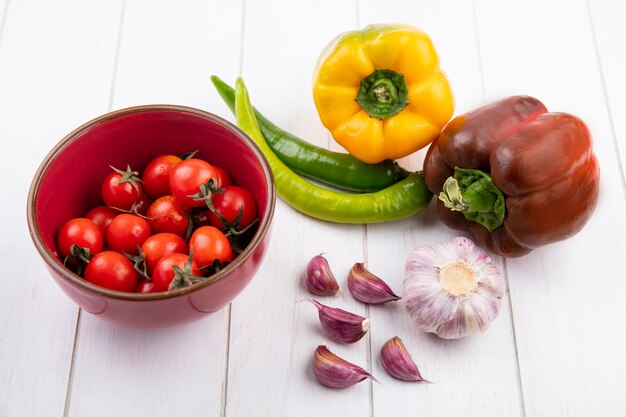 Side view of vegetables as tomatoes in bowl peppers garlic bulb and cloves on wood