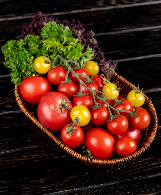 Side view of vegetables as tomatoes coriander basil in basket on wooden table