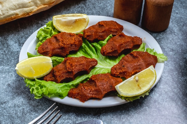 Side view vegetarian steak tartar balls with slices of lemon on lettuce leaf