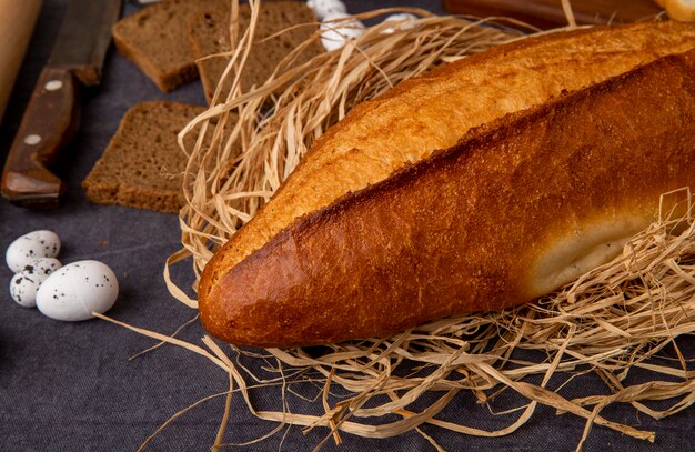 Side view of vietnamese baguette on straw and eggs with knife on maroon background