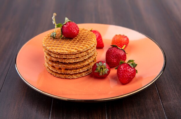 Side view of waffle biscuits with strawberries in plate on wood