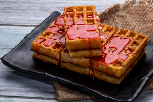 Side view of waffles with strawberry syrup on a black platter