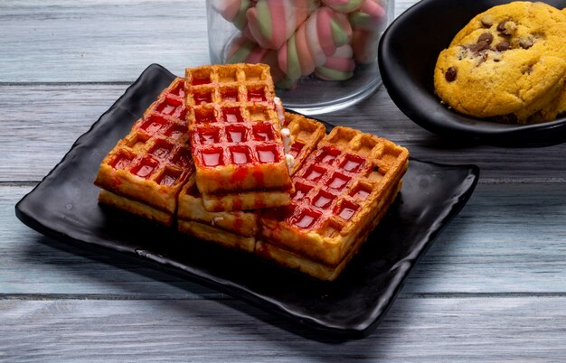 Side view of waffles with strawberry syrup on a black platter