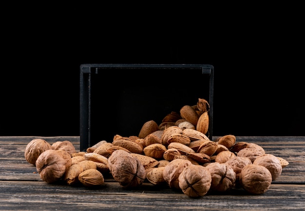 Side view walnuts and almonds from black basket on wooden horizontal