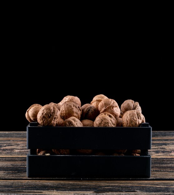 Вид сбоку грецкие орехи в черном ящике на деревянные горизонтальные