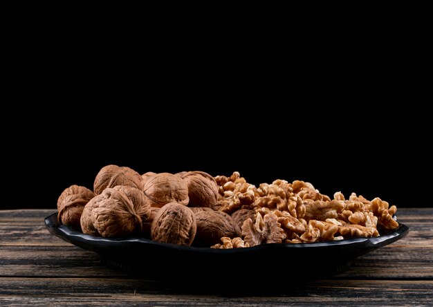 Side view walnuts in black plate on wooden table horizontal