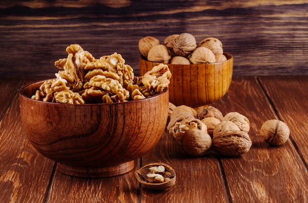 Free photo side view of walnuts in a wooden bowl on dark rustic background