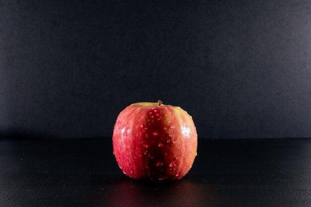 Вид сбоку мокрое красное яблоко на черном