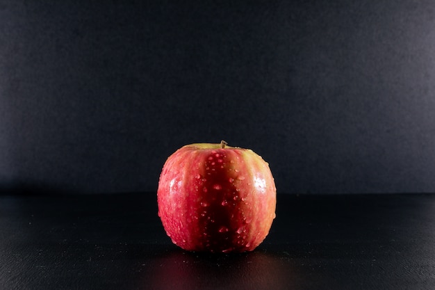 Бесплатное фото Вид сбоку мокрое красное яблоко на черном