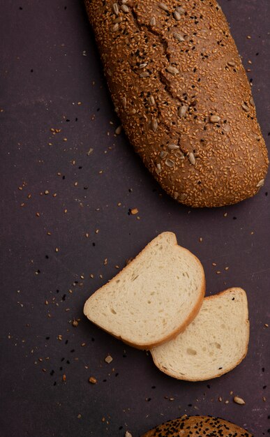 Side view of white bread slices with seeded baguette on maroon background with copy space