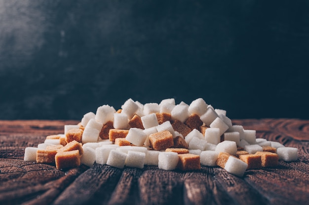 Free photo side view white and brown sugar cubes on dark and wooden table. horizontal