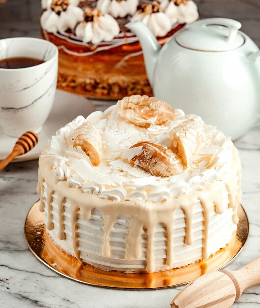 Side view of white cake decorated with melted white chocolate whipped cream and bananas on the table