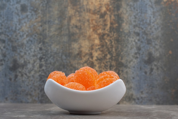 Side view of white ceramic bowl full of orange yummy candies.