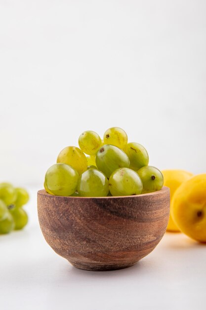 Side view of white grape berries in bowl with nectacots on white background