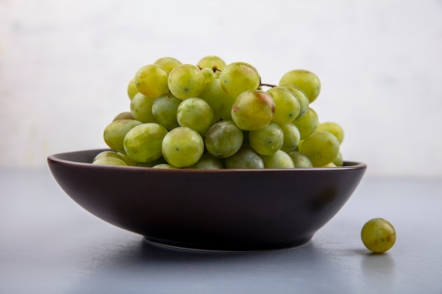 Side view of white grape in bowl on gray surface and white background