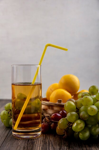 Вид сбоку белого виноградного сока с фруктами в виде нектакотов в корзине с виноградом на деревянном фоне