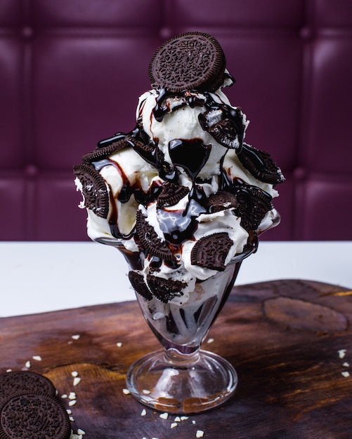 나무 테이블에 꽃병에 초콜릿 쿠키와 시럽으로 장식 된 화이트 아이스크림 국자의 측면보기