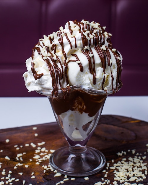 Side view of white ice cream scoops topped with chocolate and nuts in a vase on a wooden table