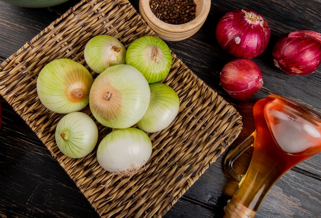 Side view of white onions in basket plate with red ones melted butter and black pepper seeds on wooden background