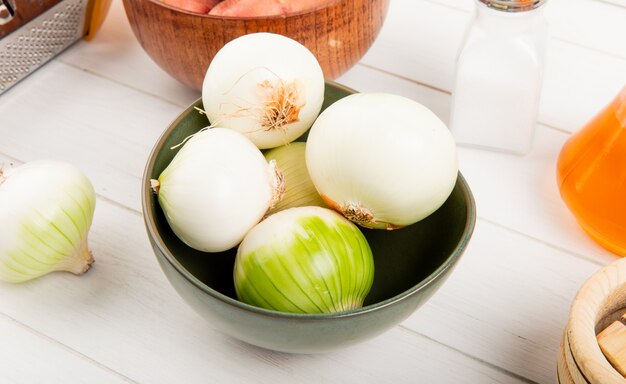 Side view of white onions in bowl with potatoes in bowl salt butter around on wooden background