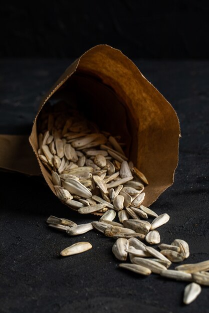 Side view of white sunflower seeds scattered from a pepper bag on black