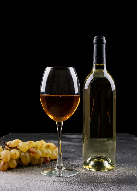 Вид сбоку белое вино с виноградом на черной вертикали
