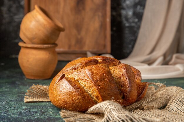 Side view of whole black bread on brown towel potteries on dark colors surface