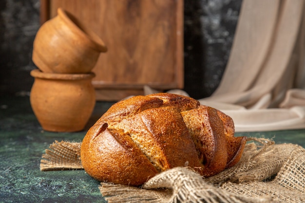 Side view of whole black bread on brown towel potteries on dark colors surface