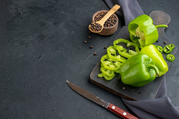 Side view of whole cut chopped green peppers on wooden cutting board on dark color surface