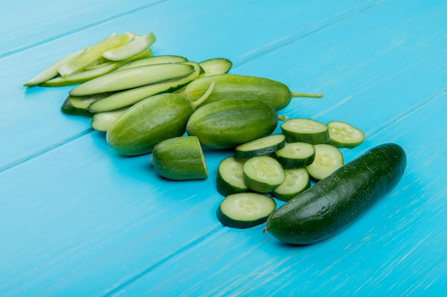 Side view of whole cut sliced cucumbers on blue surface