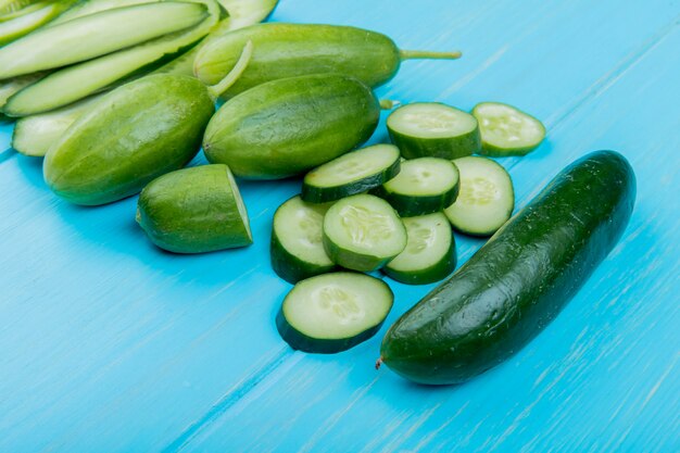 Side view of whole cut sliced cucumbers on blue surface