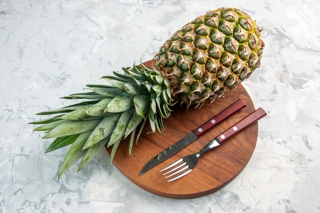 Side view of whole fresh golden pineapple fork knife on cutting board on marble surface