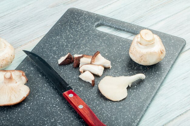 side view of whole and sliced fresh mushrooms with kitchen knife on a black cutting board on rustic table