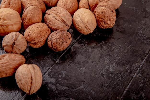 Side view of whole walnuts scattered on black wooden background with copy space