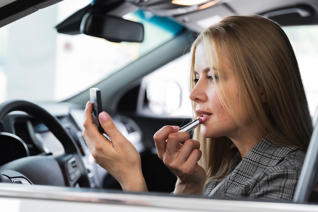 Free photo side view of woman applying lipstick