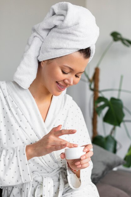 Side view of woman in bathrobe and towel using cream