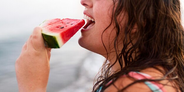 Side view of woman at the beach eating watermelon