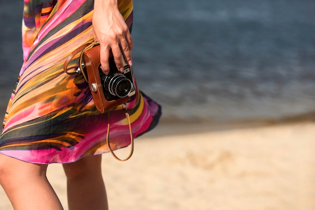 Вид сбоку женщины на пляже, держащей камеру