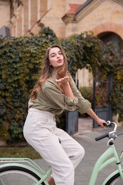 Foto gratuita vista laterale della donna che soffia bacio mentre si guida in bicicletta all'aperto