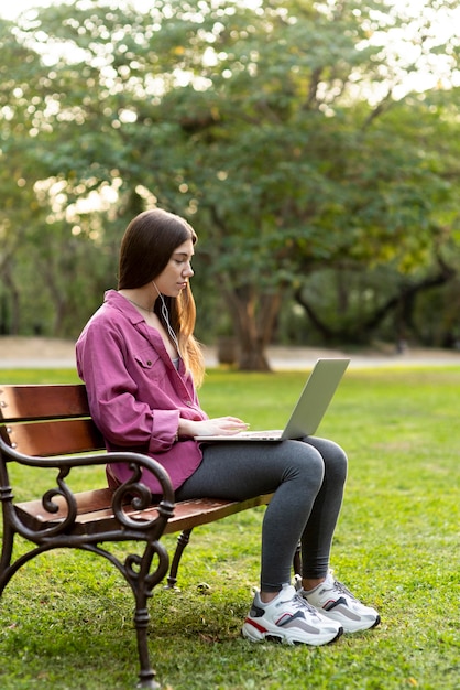 Side view woman checking her laptop on a bench