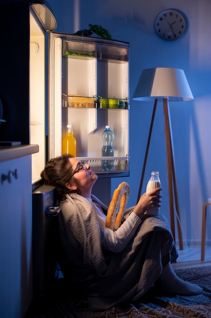 Бесплатное фото Женщина, вид сбоку, проверяет холодильник на предмет перекуса