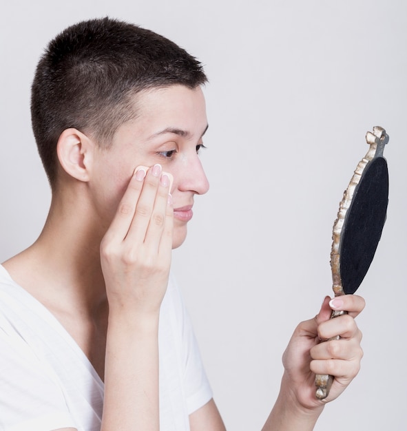 Donna di vista laterale che pulisce il suo fronte mentre guardando uno specchio