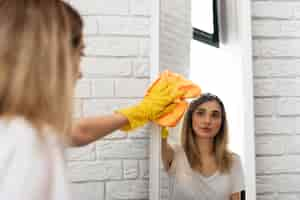 Free photo side view of woman cleaning mirror with cloth