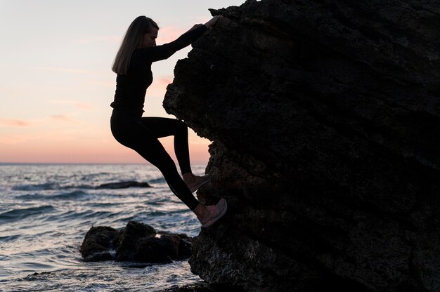 Side view woman climbing a rock next to the ocean