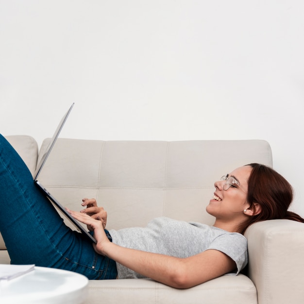 Side view of woman on couch smiling while working on laptop