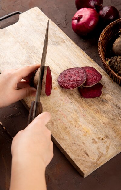 Side view woman cuts beets on a blackboard with fresh beets in a basket with red onions