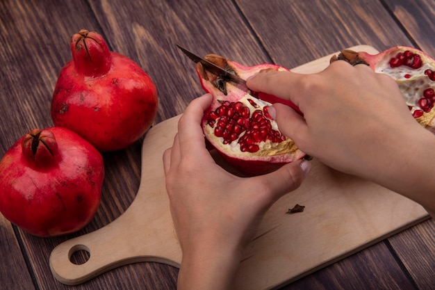 Free photo side view woman cuts pomegranate on cutting board on wooden wall