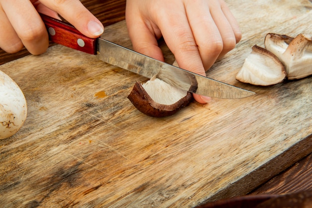 Side view of a woman cutting fresh mushrooms with a kitchen knife on a wood cutting board