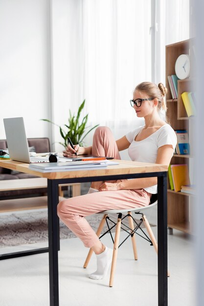 Vista laterale della donna allo scrittorio che funziona mentre a casa